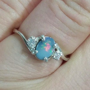 May include: A silver ring with a blue opal gemstone and two smaller clear gemstones. The ring has a curved band.