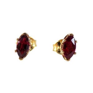 Op de afbeelding: Een paar gouden oorstekers, elk met een marquise-geslepen, dieprode edelsteen. De oorbellen hebben een klassiek ontwerp met een vier-klauwzetting, die de levendige kleur van de stenen benadrukt.