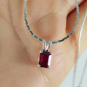 May include: A silver chain necklace with a pendant featuring a square-shaped, deep red gemstone.