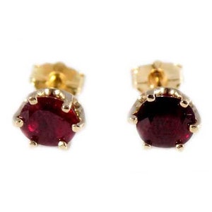 Op de afbeelding: Een paar gouden oorbelletjes met rode robijn edelstenen. De oorbelletjes hebben een simpel ontwerp met een ronde robijn die in een vier-klauw zetting zit.