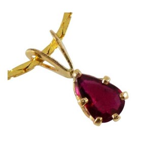 Peut inclure: Un collier doré avec un pendentif en forme de goutte d'eau, orné d'une pierre précieuse rouge foncé. Le pendentif est serti dans une lunette dorée et suspendu à une fine chaîne dorée.