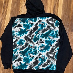 May include: Black zip-up hoodie with a tie-dye pattern on the back. The pattern features the Philadelphia Eagles logo and the word "Eagles" repeated throughout.