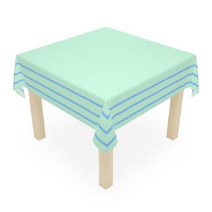 Puede incluir: Un mantel cuadrado de color verde claro con tres rayas azules horizontales. El mantel está colocado sobre una mesa cuadrada con cuatro patas de madera. La tela parece suave y ligera.