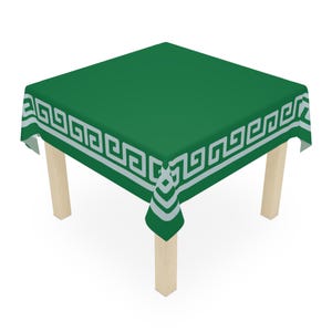 May include: A square green tablecloth with a white Greek key border is draped over a small wooden table. The tablecloth has a solid green center and a repeating geometric pattern around the edges. The table has four light-colored wooden legs.