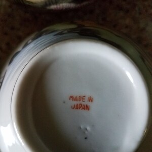 May include: A white ceramic teacup with a black and gray floral design. The bottom of the cup has the words "Made in Japan" printed in orange.