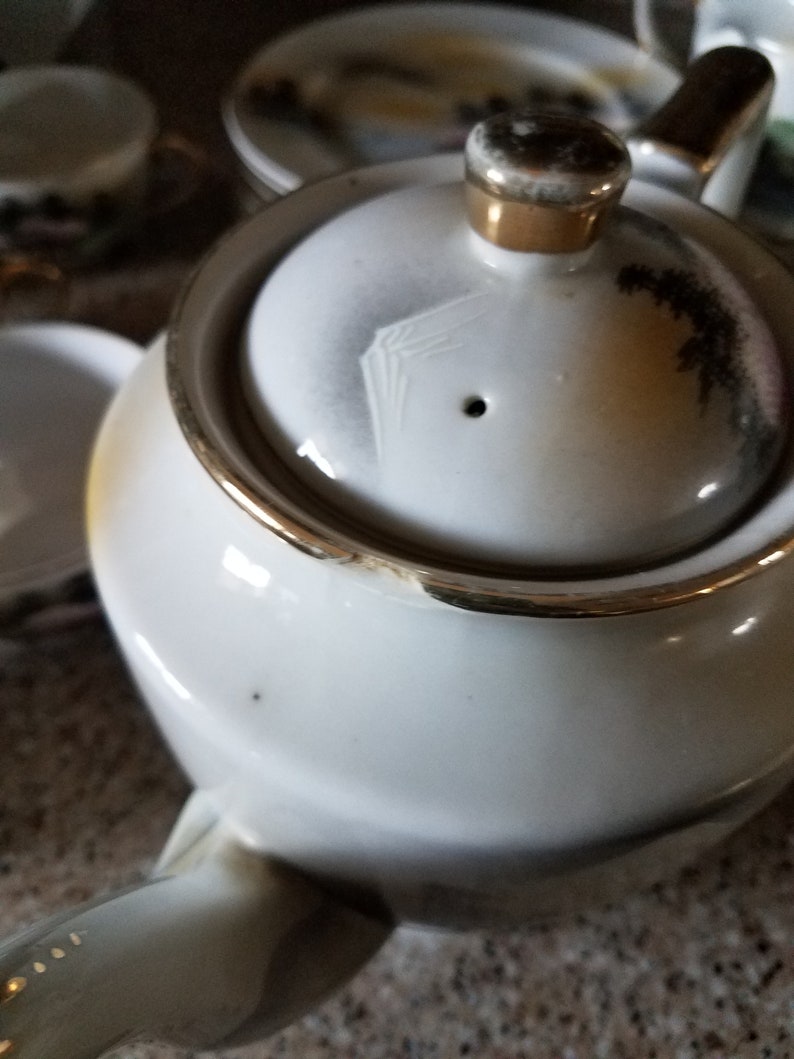 May include: White teapot with a gold trim and a lid with a floral design. The teapot has a spout and a handle.