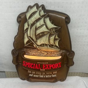 May include: A vintage Heileman's Special Export Beer sign featuring a detailed sailing ship. The sign is brown with a light-up section displaying the text "SPECIAL EXPORT BEER". The text "You can travel the world over and never find a better beer" is also included.