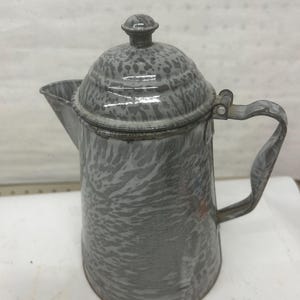 May include: A vintage gray and white speckled enamelware coffee pot with a lid and handle. The pot has a spout for pouring and a classic design, perfect for kitchen decor or collectors.