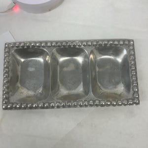 Könnte beinhalten: Ein rechteckiges, silberfarbenes Serviertablett mit drei Fächern. Das Tablett hat einen Perlenrand und ein leicht angelaufenes Aussehen. Ideal zum Servieren von Vorspeisen oder Gewürzen.