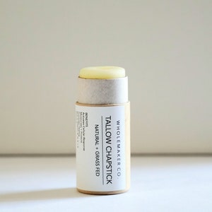 May include: A natural tallow chapstick in a cylindrical cardboard tube. The label reads "TALLOW CHAPSTICK NATURAL + GRASS FED" with the brand name "WHOLEMAKER CO." and the benefits listed. The chapstick itself is a light yellow color.