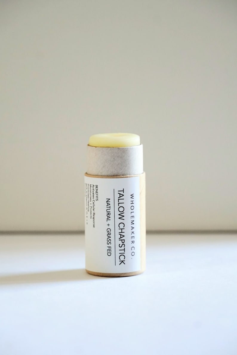 May include: A natural tallow chapstick in a cylindrical cardboard tube. The label reads "TALLOW CHAPSTICK NATURAL + GRASS FED" with the brand name "WHOLEMAKER CO." and the benefits listed. The chapstick itself is a light yellow color.