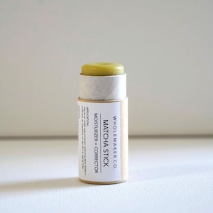May include: A cylindrical Matcha Stick moisturizer and corrector by Wholemaker Co. The product has a light green top and is encased in a cardboard tube with product information. The text on the label reads "Matcha Stick Moisturizer + Corrector".