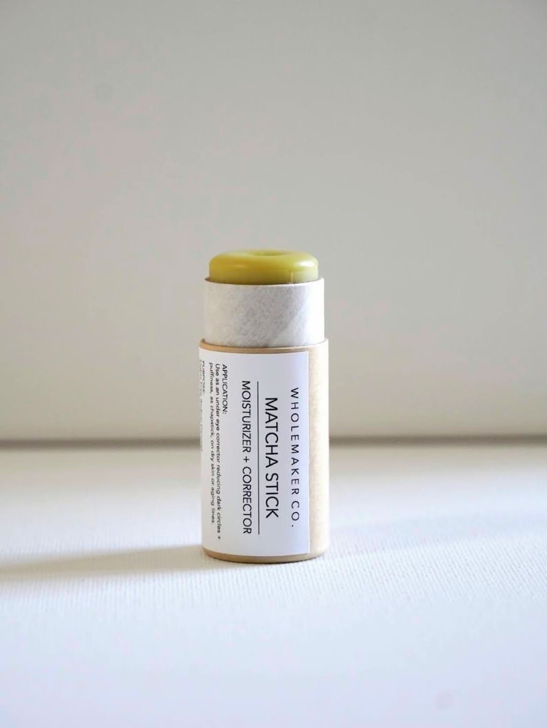 May include: A cylindrical Matcha Stick moisturizer and corrector by Wholemaker Co. The product has a light green top and is encased in a cardboard tube with product information. The text on the label reads "Matcha Stick Moisturizer + Corrector".