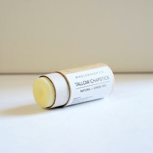 May include: A cylindrical tallow chapstick with a light yellow balm. The product is in a cardboard tube with a white label that reads "Tallow Chapstick Natural + Grass Fed" and "Whole Maker Co."