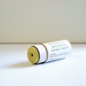 May include: A matcha stick moisturizer and corrector in a cylindrical cardboard tube. The product is light green and has a hole in the center. The text "WHOLEMAKER CO." and "MATCHA STICK" are printed on the tube.
