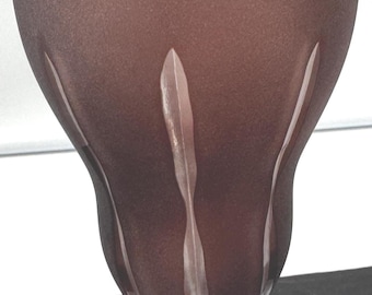 May include: A tall, frosted, burgundy-colored glass with a wide rim and a flared, tulip-shaped body. Vertical, leaf-like designs are etched into the glass, adding a decorative element. The glass sits on a small, round, frosted base.
