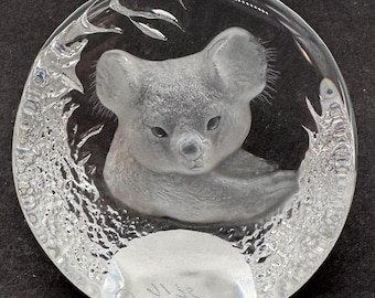 May include: A clear glass paperweight featuring a detailed, three-dimensional sculpture of a koala bear. The koala is resting on its belly with its head turned to the side. The paperweight is signed "VI 42".