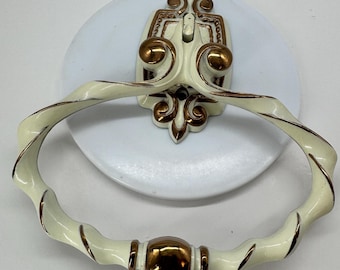 May include: A wall-mounted towel ring featuring an off-white finish with metallic bronze accents. The mounting plate has an ornate, symmetrical design with scrollwork, while the ring itself has a twisted, rope-like texture and a central accent.