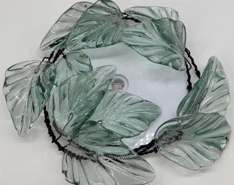 May include: A circular garland featuring translucent, pale green glass leaves with detailed vein textures. The leaves are strung together on a thin, black twisted wire cord, creating a continuous loop of decorative foliage elements.