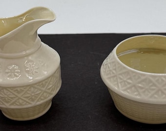 May include: A cream-colored ceramic creamer and sugar bowl set with an intricate embossed pattern. The set features a delicate floral design and a woven basket pattern.