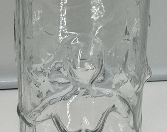 May include: A tall, cylindrical clear glass vase featuring a textured, uneven surface. The exterior of the glass is molded with a relief design of a stylized human figure with arms outstretched, integrated into the body of the vessel.