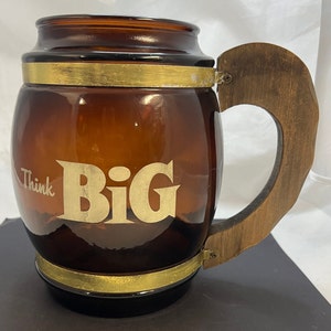 May include: A brown glass beer stein with a wooden handle. The stein has a gold band around the top and bottom and the words "Think Big" etched on the front.