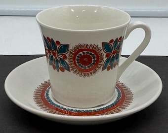 May include: A white teacup and saucer with a colorful floral pattern in shades of red, orange, blue, and green. The pattern features stylized flowers and leaves.