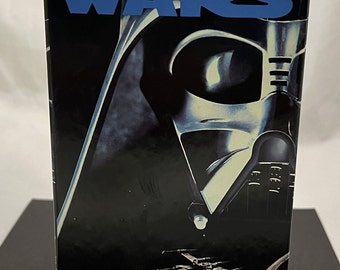 May include: A VHS tape case for the Star Wars Trilogy. The case features a black and white image of Darth Vader's helmet. The text "STAR WARS TRILOGY" is printed in blue on the top of the case. The text "DIGITALLY MASTERED FOR SUPERIOR SOUND THX AND PICTURE QUALITY" is printed in white on the bottom of the case.