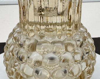 May include: A clear glass vase with a spherical body featuring a raised honeycomb or bubble texture. The neck of the vase is cylindrical with vertical ribbed detailing. The glass has a subtle amber or champagne tint throughout the entire structure.