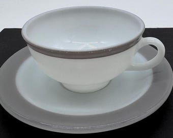 May include: A white teacup and saucer set with a gray band around the rim of each piece.
