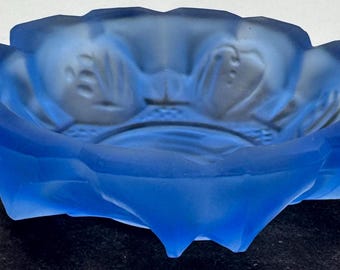 May include: A blue glass ashtray with a floral design. The ashtray is made of frosted glass and has a scalloped edge.