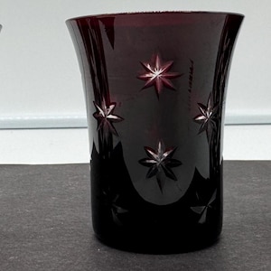 Puede incluir: Tres vasos de vidrio rojo oscuro con diseños de vidrio cortado. Los vasos tienen diferentes patrones, uno con un patrón de diamante, otro con un patrón de estrella y otro con una combinación de ambos.