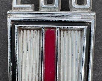 May include: A chrome emblem with the number 230 and a red and silver shield with vertical lines.
