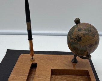 May include: A wooden desk organizer with a globe and a pen holder. The globe is a small, antique-style globe with a brown and cream colored map. The pen holder is a slot in the wood. The organizer is made of a light brown wood.