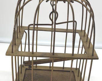 May include: A square brass birdcage featuring a domed top with a circular hanging loop, vertical wire bars, a central horizontal perch, and a flat base with a decorative row of small circular cutouts along the bottom edge of the frame.