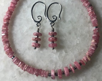 May include: A set of pink gemstone jewelry featuring a bracelet and earrings. The bracelet is made of small, flat, pink stones with silver accents. The earrings are silver with three pink stones each.