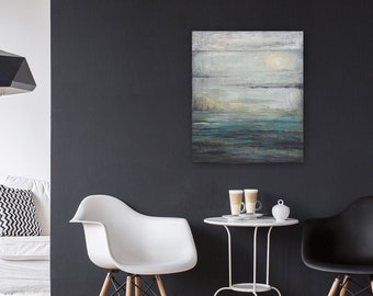 Op de afbeelding: Een witte bank met een zwart-wit gepatroneerd kussen staat in een woonkamer met een witte bijzettafel en een zwarte hanglamp. Twee stoelen, een witte en een zwarte, staan voor een zwarte muur met een schilderij van een zeegezicht en een klok. Een witte tafel met twee kopjes koffie staat tussen de stoelen.