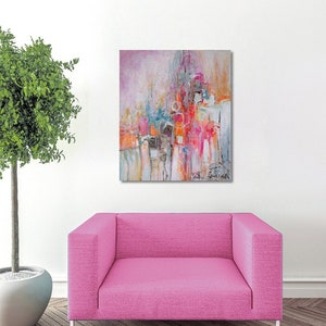 Op de afbeelding: Abstract schilderij met roze, oranje en blauwe kleuren. Het schilderij hangt aan een witte muur boven een roze fauteuil.