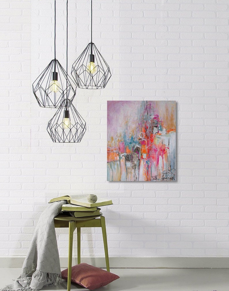 Op de afbeelding: Abstract schilderij met roze, oranje en blauwe tinten. Het schilderij hangt aan een witte bakstenen muur met drie zwarte geometrische hanglampen erboven.