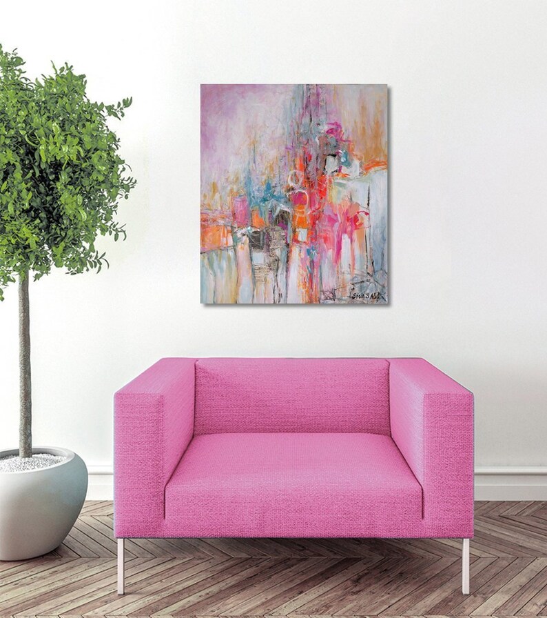 Op de afbeelding: Abstract schilderij met roze, oranje en blauwe kleuren. Het schilderij hangt aan een witte muur boven een roze fauteuil.