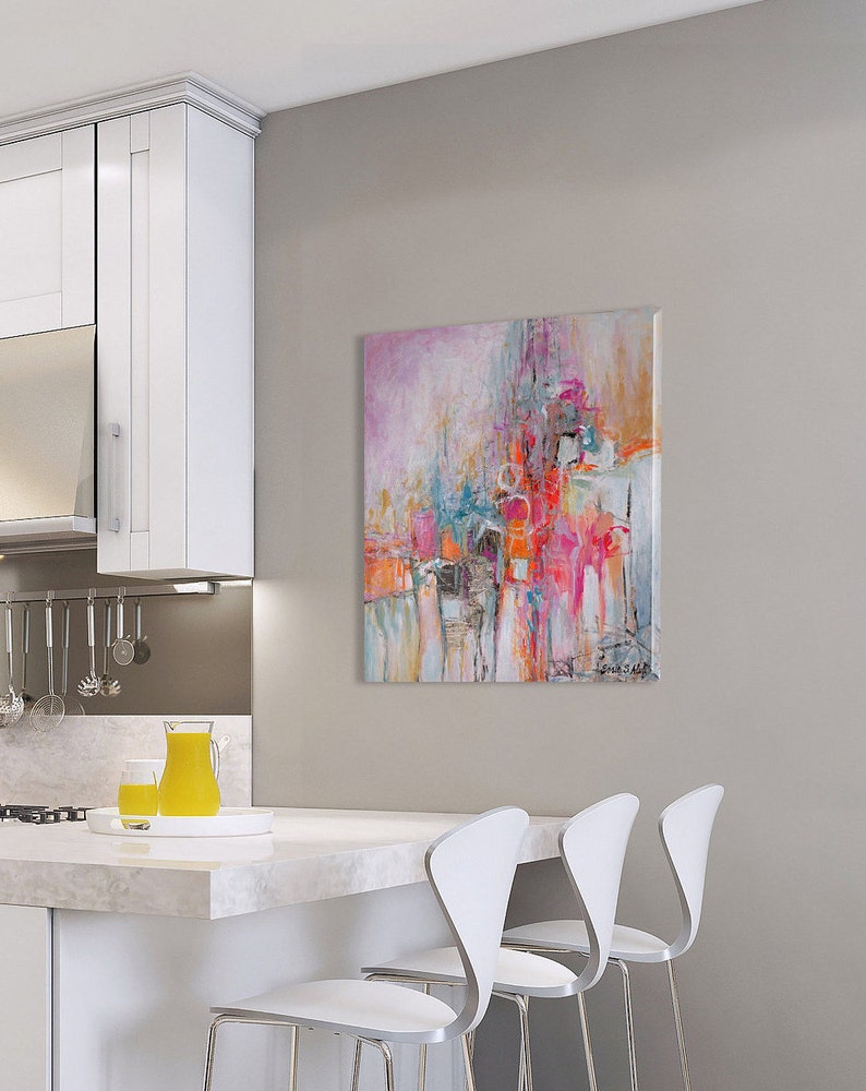 Op de afbeelding: Abstract schilderij met roze, oranje, blauwe en witte kleuren. Het schilderij hangt aan een muur in een keuken met witte kasten en een wit aanrecht.