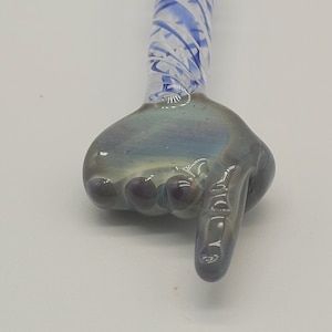 May include: A glass hand pipe with a blue and white swirl design. The hand is pointing to the right.
