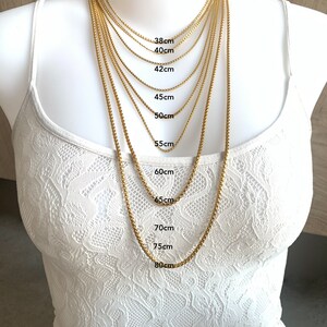 May include: A gold chain necklace in various lengths from 38 to 80 centimeters. The necklace is displayed on a white mannequin.