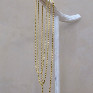 May include: Four gold rope chains of varying lengths hanging from a white wooden stand.