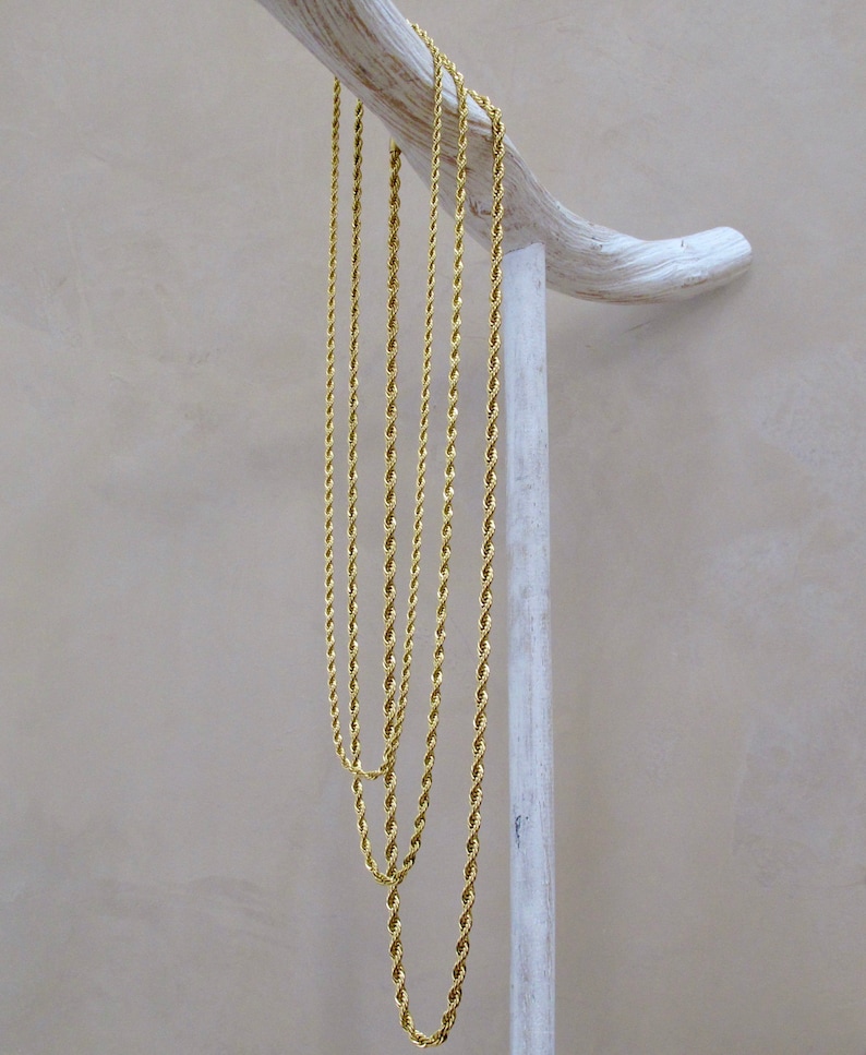 May include: Four gold rope chains of varying lengths hanging from a white wooden stand.
