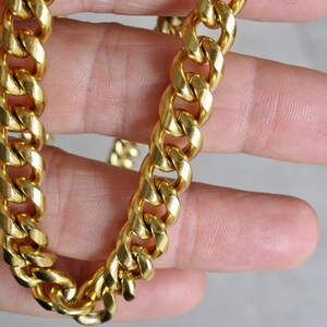 May include: A gold chain necklace with a curb link style. The chain is thick and has a shiny finish.