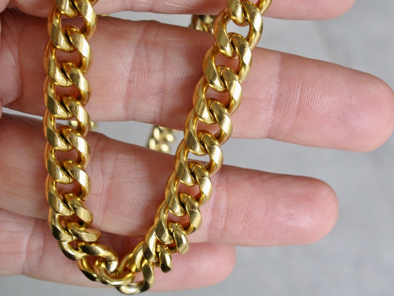 May include: A gold chain necklace with a curb link style. The chain is thick and has a shiny finish.