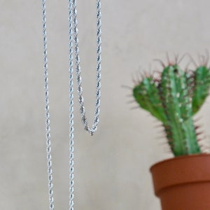 May include: Two silver rope chains hanging against a light beige background. The chains are made of a twisted rope design.
