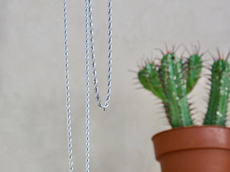 May include: Two silver rope chains hanging against a light beige background. The chains are made of a twisted rope design.