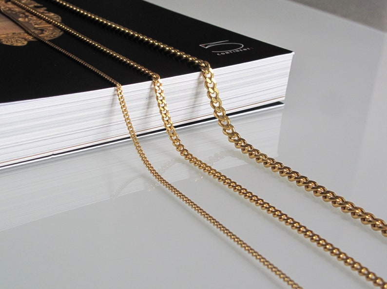 May include: Four gold chains of different thicknesses and styles, laid out on a white surface. The chains are arranged in order of size, with the thickest chain at the top and the thinnest chain at the bottom.